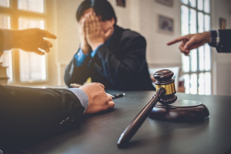 A stressed individual at a table with a gavel, illustrating the urgency of getting legal representation before indictment.